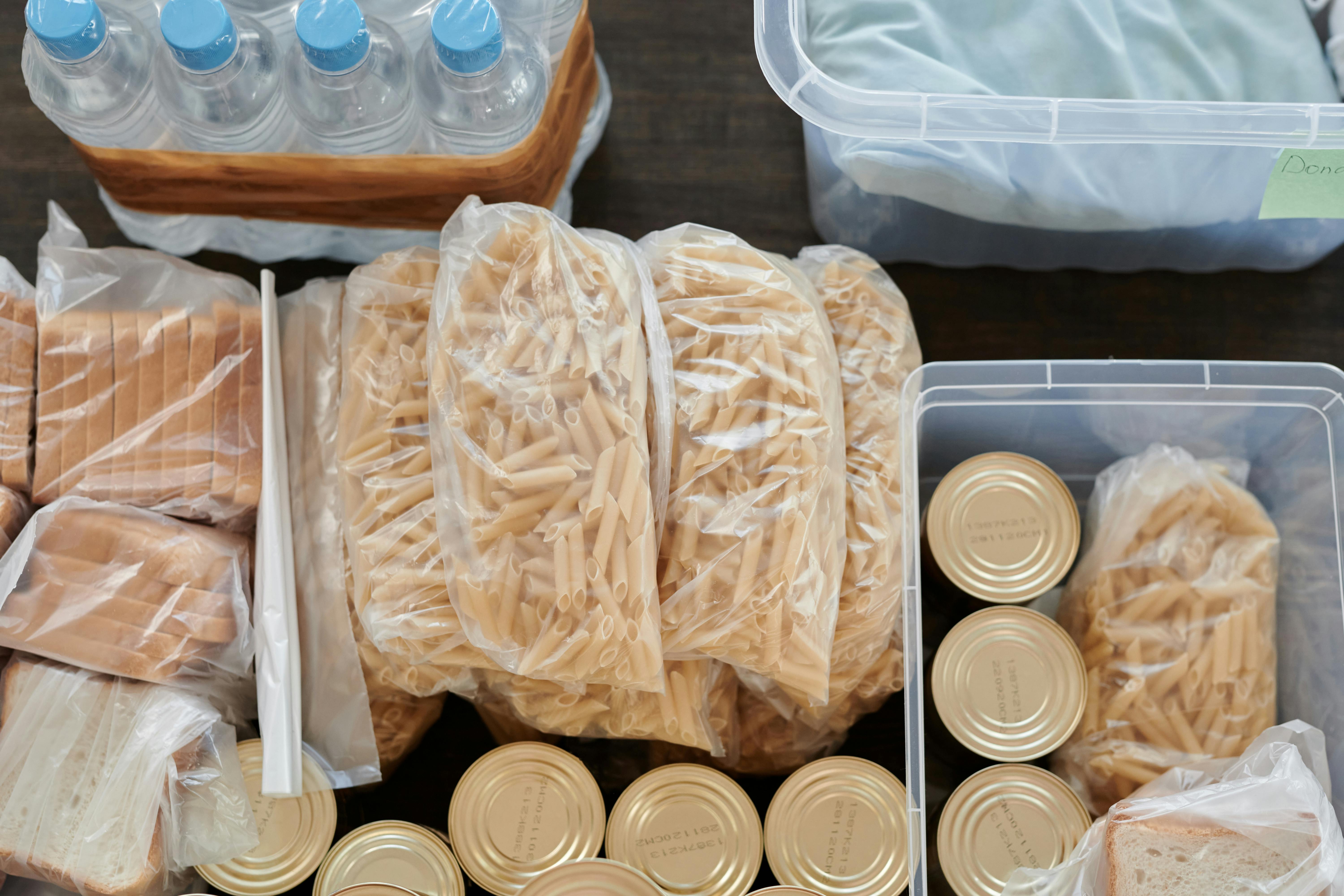 Aerial shot of pantry essentials including pasta, canned food, and bread packaged in plastic bags.