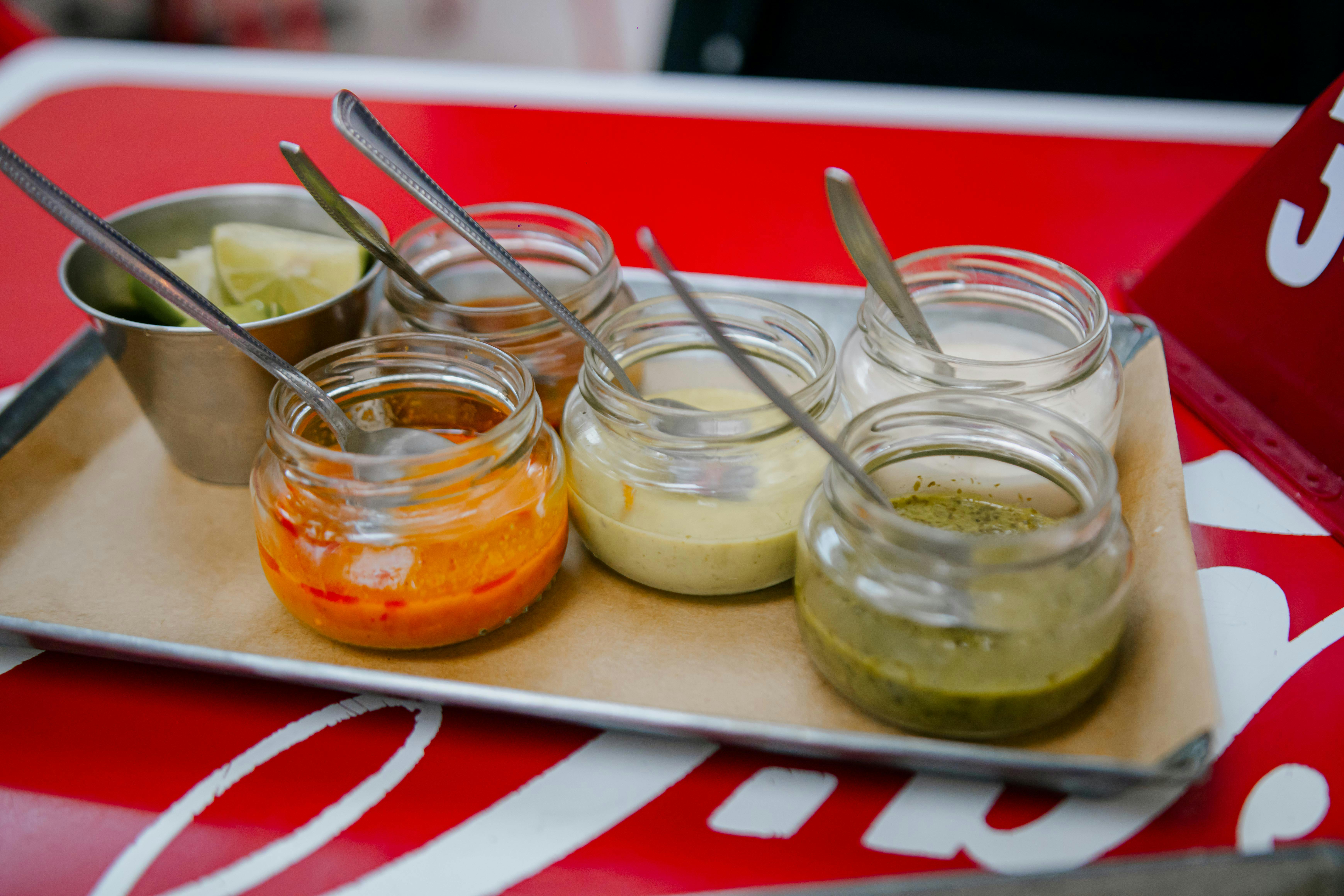 Close-up of colorful sauces in glass jars with spoons on a tray, perfect for culinary presentations.