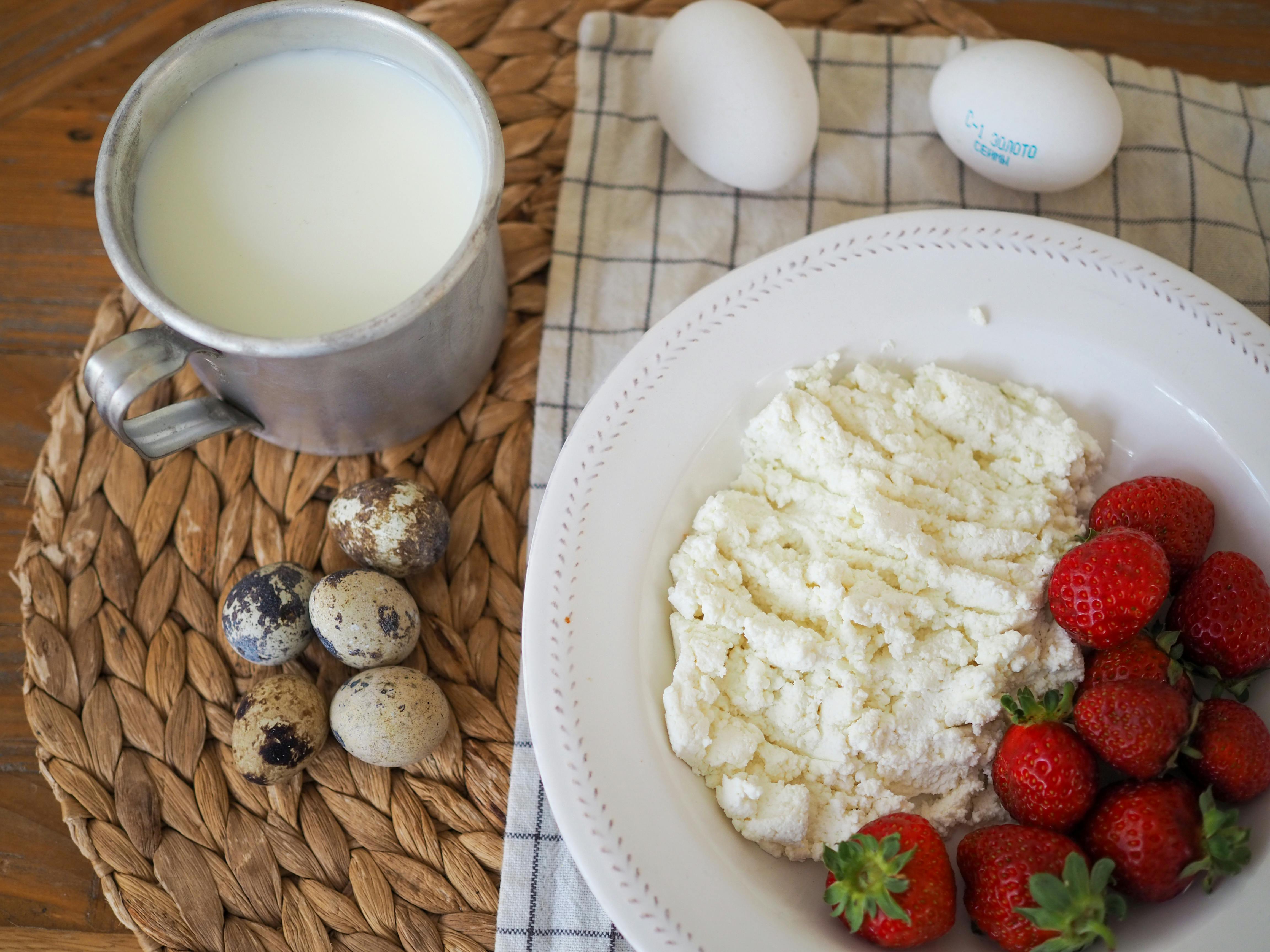 Top view of a rustic breakfast with milk, quail eggs, cottage cheese, and strawberries on a woven mat.