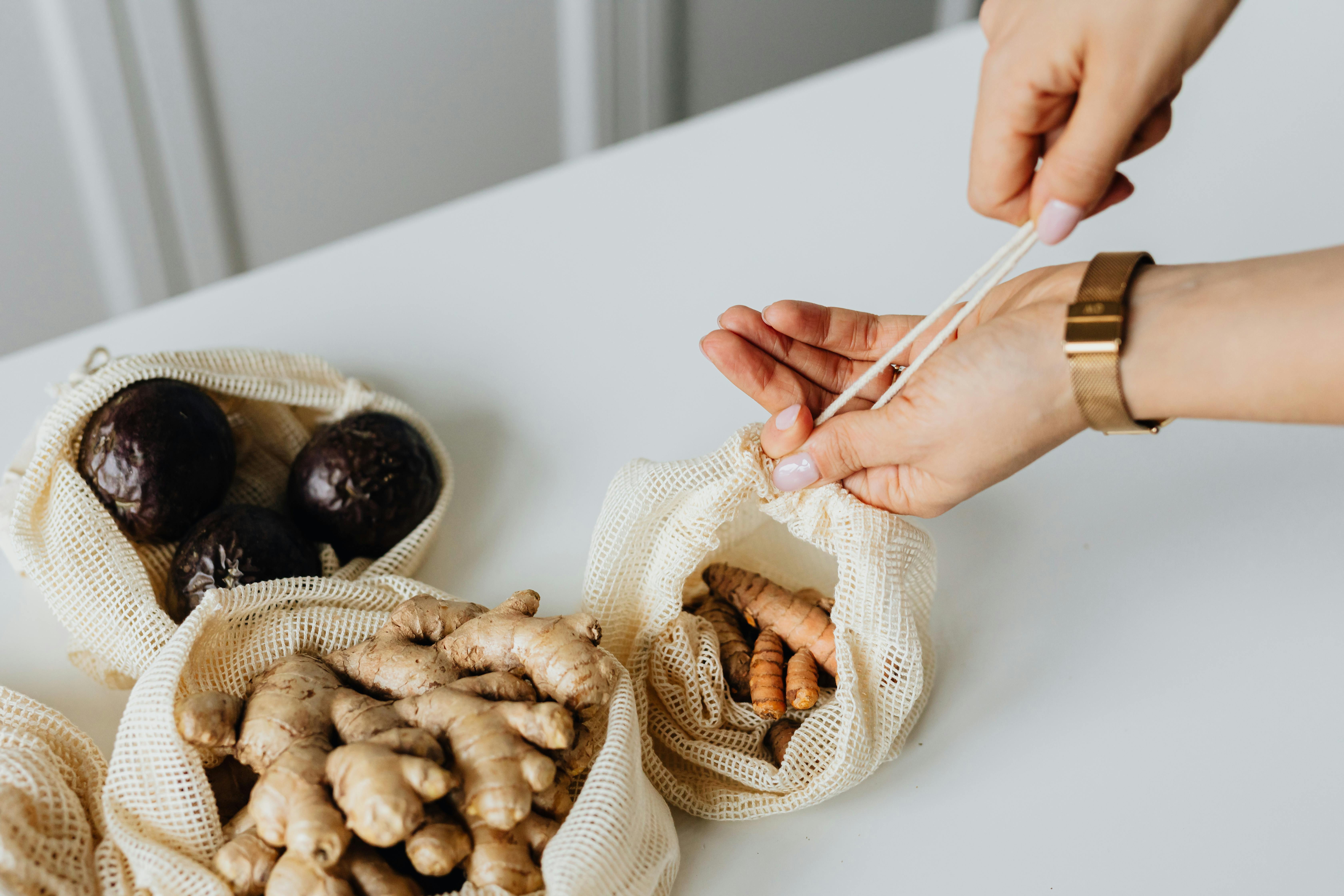 Close-up of hands using eco-friendly mesh bags filled with fresh ginger and avocados.