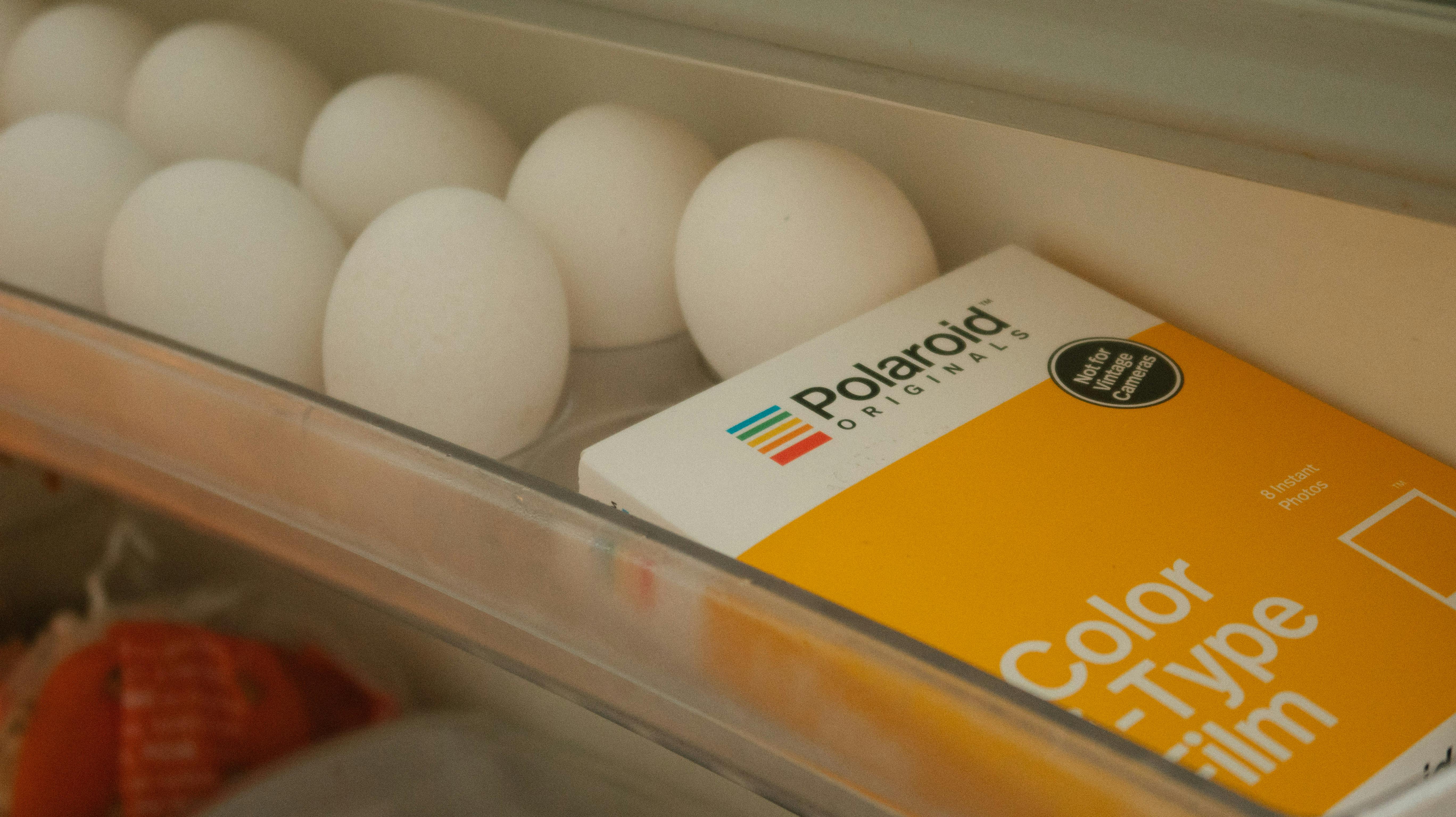 Close-up of fresh eggs and Polaroid film box in refrigerator, symbolizing freshness and nostalgia.