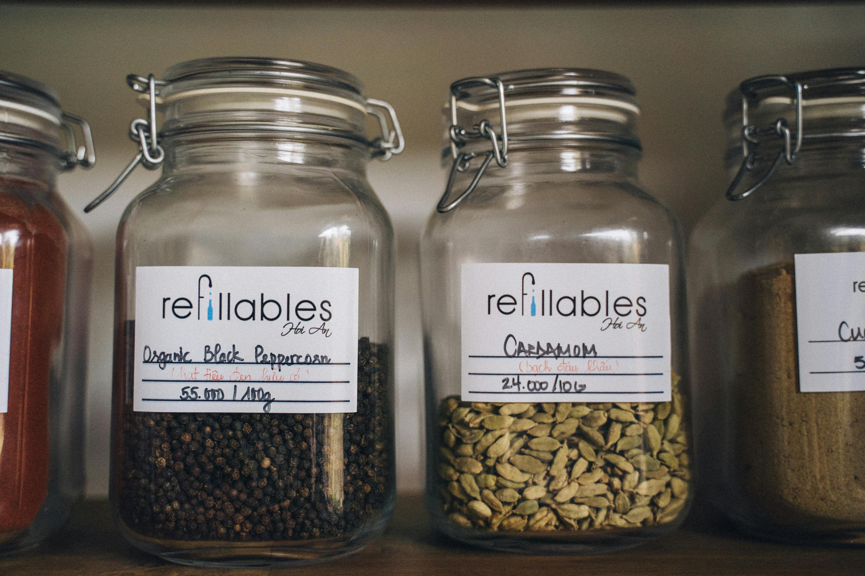 A collection of spices in eco-friendly refillable glass jars on a wooden shelf, promoting sustainable food storage.