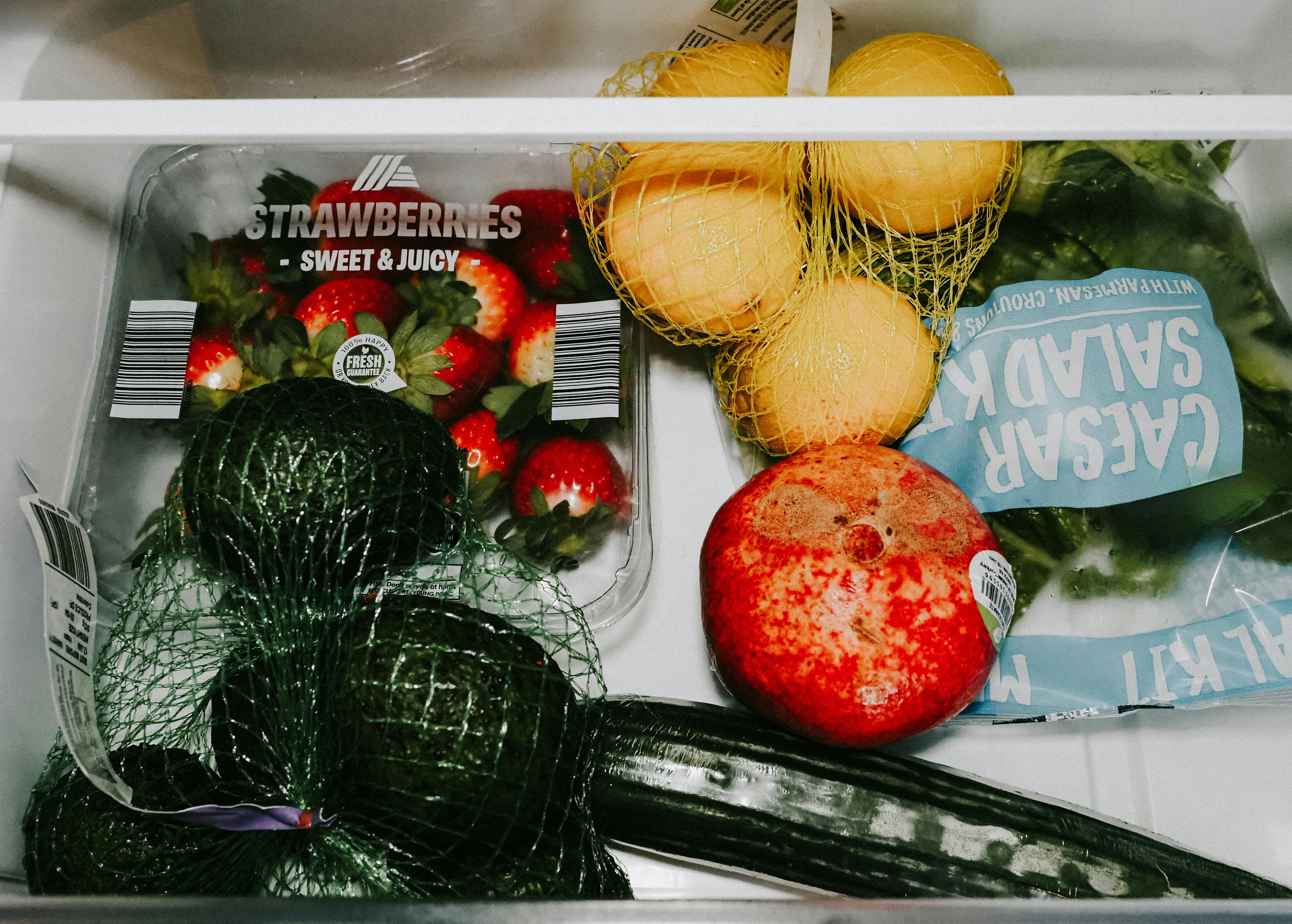 A variety of fresh fruits and vegetables including avocados, lemons, strawberries, and lettuce in a fridge drawer.