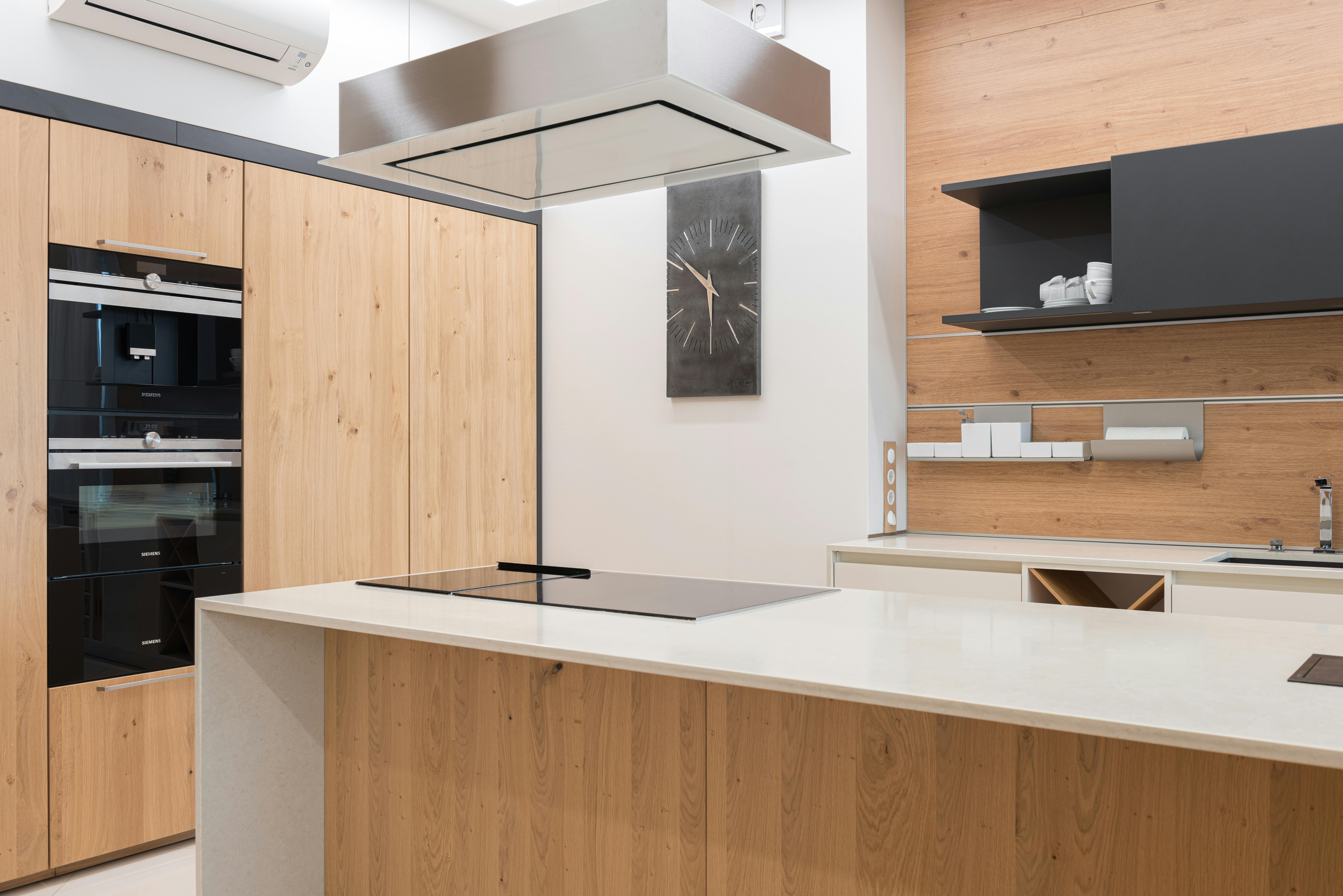 Interior of modern kitchen with built in oven and stove near contemporary black clock hanging on wall